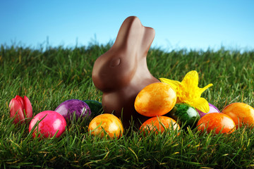 Milk chocolate easter bunny and colorful eggs in fresh green grass - healthy picnic concept