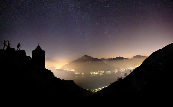 Lake of Como by night from the church of Saint Bernardo of Musso with some photographers intent on taking pictures..Church of saint Bernardo, .Musso, .Lake of Como, .Lombardy,.Italy.