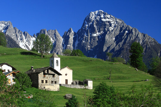 Spring view of the church and the chalets of Dal&Atilde;&sup2; with behind the majestic Prata Peak. Valchiavenna. Valtellina. Vallespluga. Lombardy. Italy. Europe.