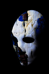 Textured mask with cracked rough wood  painted surface, neutral expression on dark background.