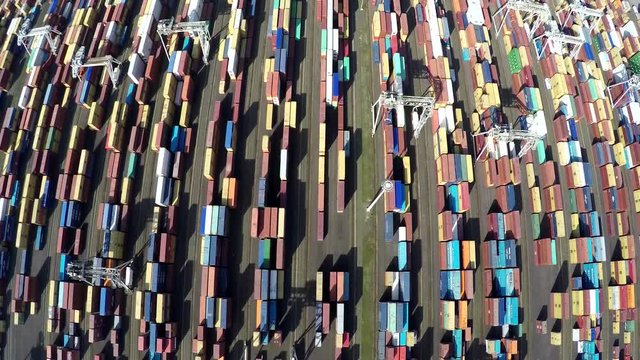 Aerial top down view flying straight over container terminal showing many intermodal containers used for freight transport shipping goods stacked up on each other different colors harbor area 4k