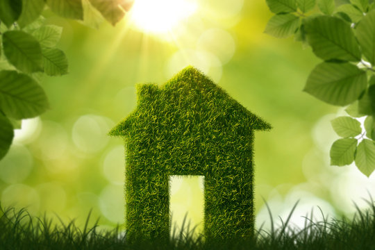 Grass house symbol over green defocused background with copy space