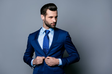 Portrait of serious fashionable handsome man in blue suit and tie buttoning jacket