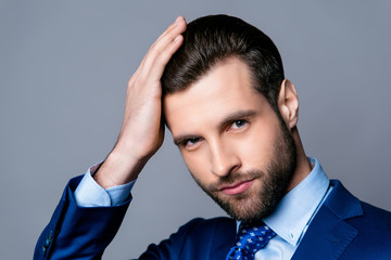 Close up portrait of serious handsome man in blue suit and tie touching his perfect hair