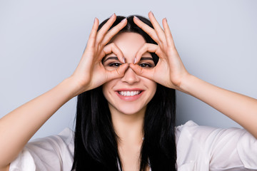 Young cheerful laughing woman having fun and making binoculars using her hands isolated on gray background