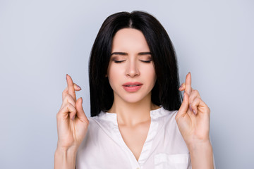 Portrait of young minded woman in white shirt with closed  eyes and crossed hands waiting for success