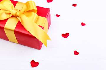 Gift box with red satin hearts. Present wrapped with yellow ribbon. Christmas or birthday package. On white wooden table.