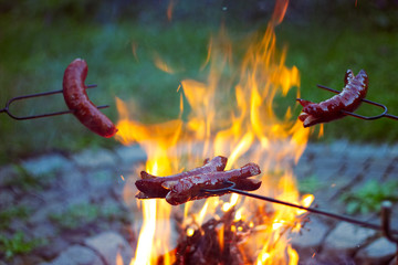 Grilling sausages over a campfire, campers roasting sausages on toasting forks 