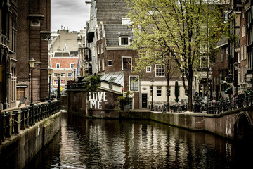 Fototapeta premium Houses along a canal in Amsterdam. Reflection in the water. Graffiti on the wall.