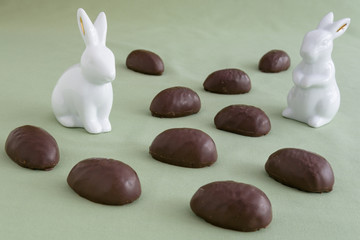 Two white ceramic Easter bunnies in a field of chocolate covered marshmallow eggs on a green background
