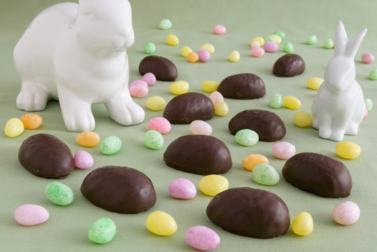 Two white ceramic Easter bunnies in a field of chocolate covered marshmallow eggs and colorful jelly beans
