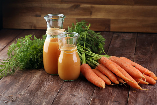 Fresh carrot juice in bottles and carrots on a grey wooden table