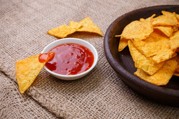 Nachos chips. Delicious salty tortilla with sweet salsa or chilli sauce on sackcloth background. Snack on rustic plate.