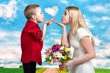  Young beautiful mother and son blow kisses .A woman and a boy with a bouquet,a basket of flowers.               Spring concept of family vacation and family love. Women's day