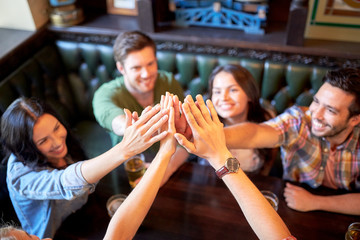friends drinking beer and making high five at bar
