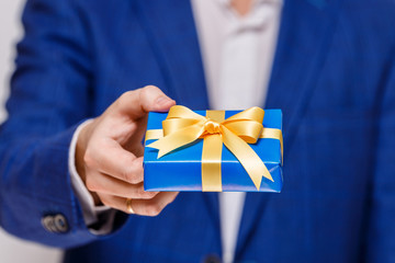 Male hand holding a gift box. Present wrapped with ribbon and bow. Christmas or birthday blue package. Man in suit and white shirt.
