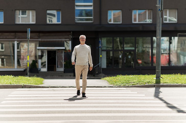 senior man walking along city crosswalk