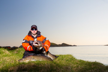 fisherman man sits on the shore with a huge fish in his hands. Evening. Dirty clothes.