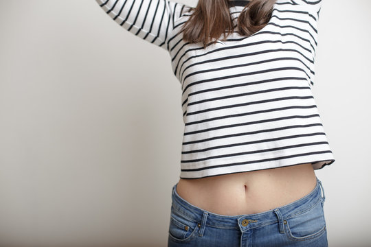 Young girl in blue jeans and a striped sweater and lifted her arms bare belly with a beautiful waist and umbilicus