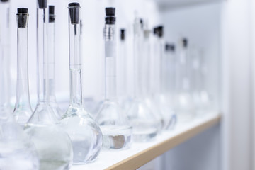 Flasks with liquid chemicals stand on a shelf in a real laboratory