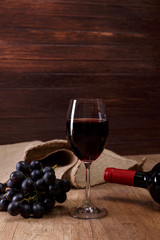 Red wine. Bottle and Wineglass with dark grapes branch. On rustic wooden background.