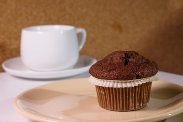 Chocolate cupcake on brown plate, white coffee cup in background
