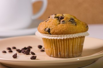 Vanilla muffin served on a plate with teacup in the background and chocolate chips as decoration