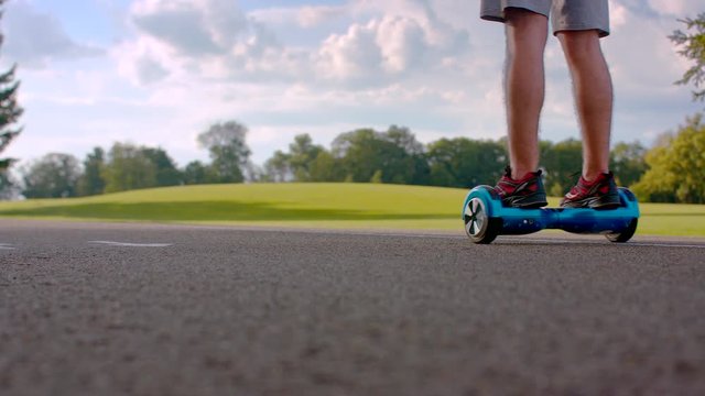 Man riding on gyro scooter on asphalt road. Back view of man driving self balancing board. Closeup of man legs on electric gyroscooter in park. Man using modern electric transport on road