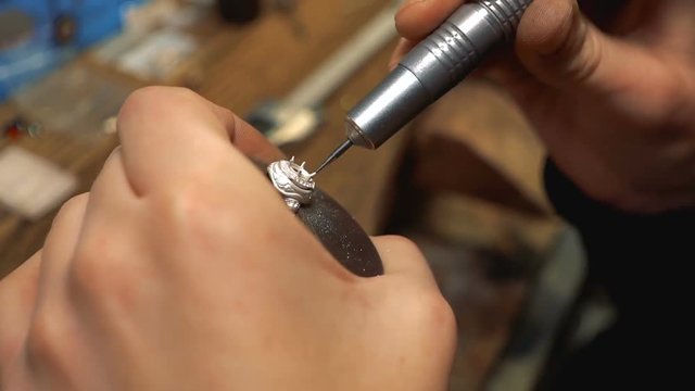 Jewelry master turns the silver ring in the vice and drills a hole for the inlay of the gemstones