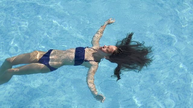 Teen Girl In Swiming Suit Lay On Swimming Pool Water With Long Hair Floating On Surface