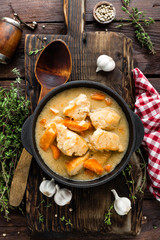 Meat stewed with carrots in sauce and spices in cast iron pan on dark wooden rustic background top view flat lay