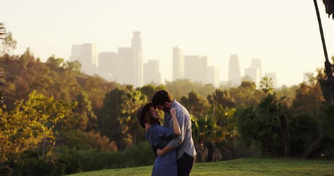 Couple kiss in slow motion, tilt up LA cityscape in background