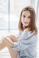 Closeup portrait of young smiling Caucasian woman  with long red blonde hair in blue shirt pajama sitting in bed after waking up, indoors at home early morning, lifestyle