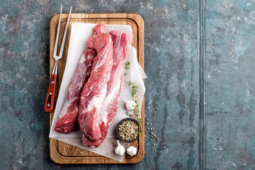 Fresh raw pork tenderloin on wooden cutting board on dark background