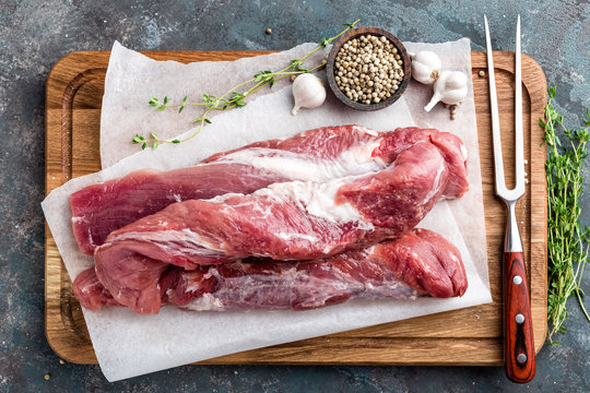 Fresh raw pork tenderloin on wooden cutting board on dark background
