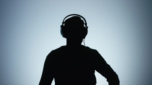 Half length silhouette portrait of bearded Caucasian male putting on headphones and listening to music on his phone against white background. 4K UHD 60 FPS slow motion