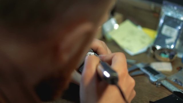 Artist makes inlay of a silver ring close-up and holds a vise in his hand