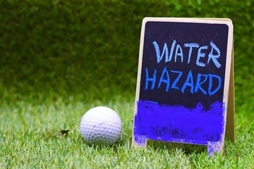 Water Hazard sign and golf ball are on green grass