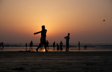 Silhouettes of locals playing beach cricket at sunset in India
