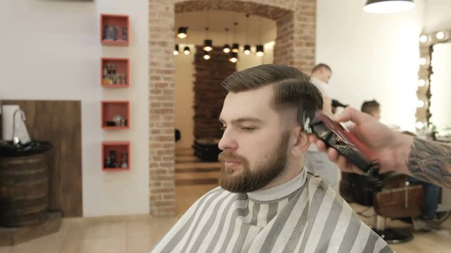 portrait of handsome man with beard in barbershop. barber working with electric razor. Background salon barbershop