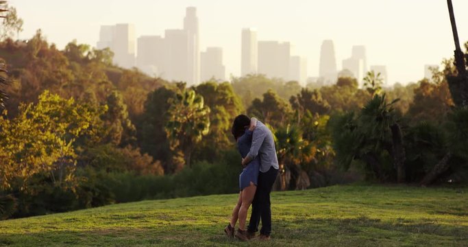 Wide shot, man and woman kiss in slow motion, LA cityscape in background