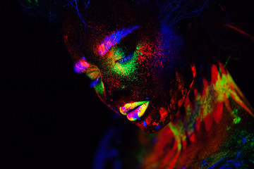 Beautiful extraterrestrial model woman in neon light. It is portrait of beautiful model with fluorescent make-up, Art design of female posing in UV with colorful make up. Isolated on black background