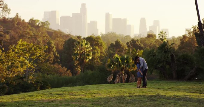 Man and woman kiss in slow motion, wide shot with LA cityscape in background