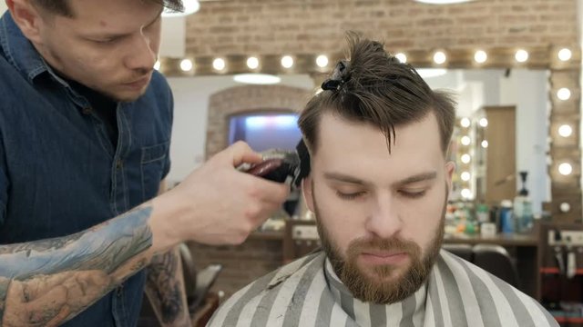 Men's Hairdressers barbers. Barber cuts the client machine for haircuts. Tattoos on the hands