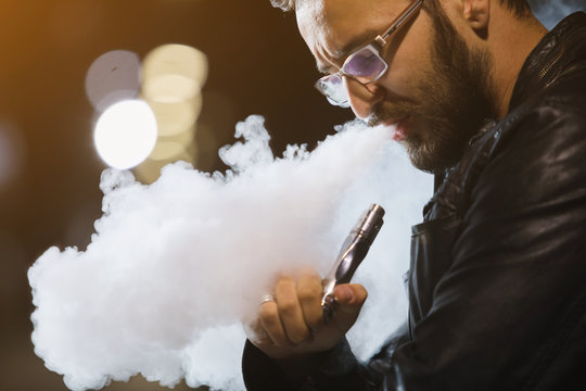 Vaping man holding a mod. A cloud of vapor. Stylish hipster with vape.