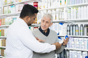 Fototapeta na wymiar Pharmacist Assisting Senior Customer In Buying Product