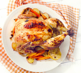 Whole roasted chicken with vegetables on a white plate.