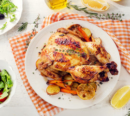Whole roasted chicken with vegetables and salad on a wooden background.