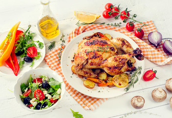 Roasted chicken with vegetables and salad on a white wooden background.