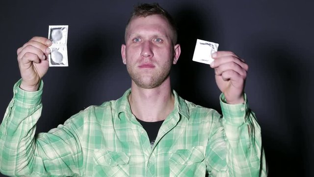 
4K. Man  show  condoms on palm in front of dark background.
